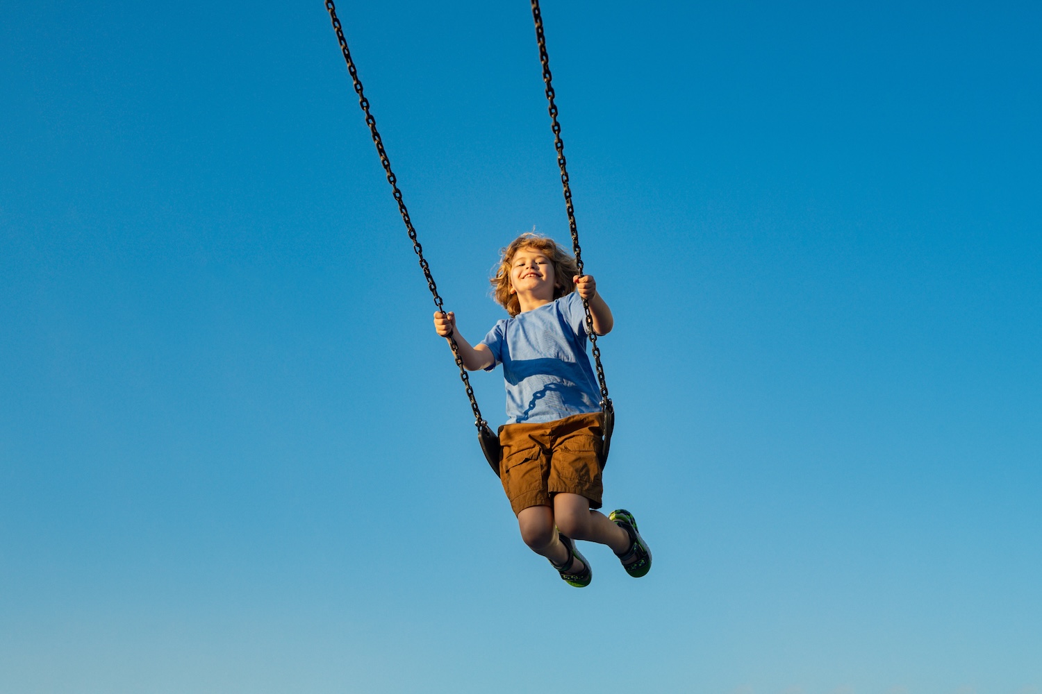 Cute child having fun on a swing on a blue summer sky background. 