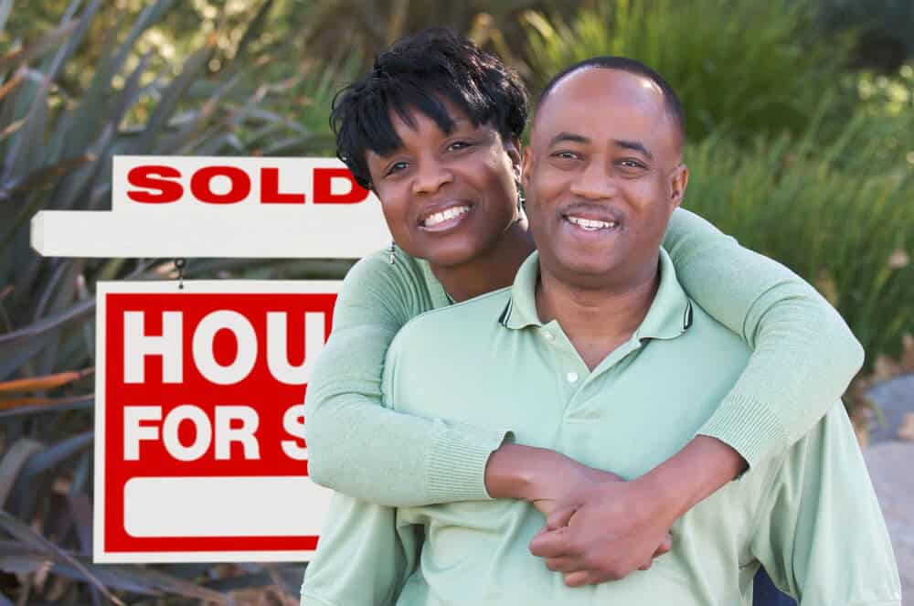 An African American couple in front of a sold house for sale sign. Alternative ways to buy a house in Louisiana helps homebuyers get into a house.